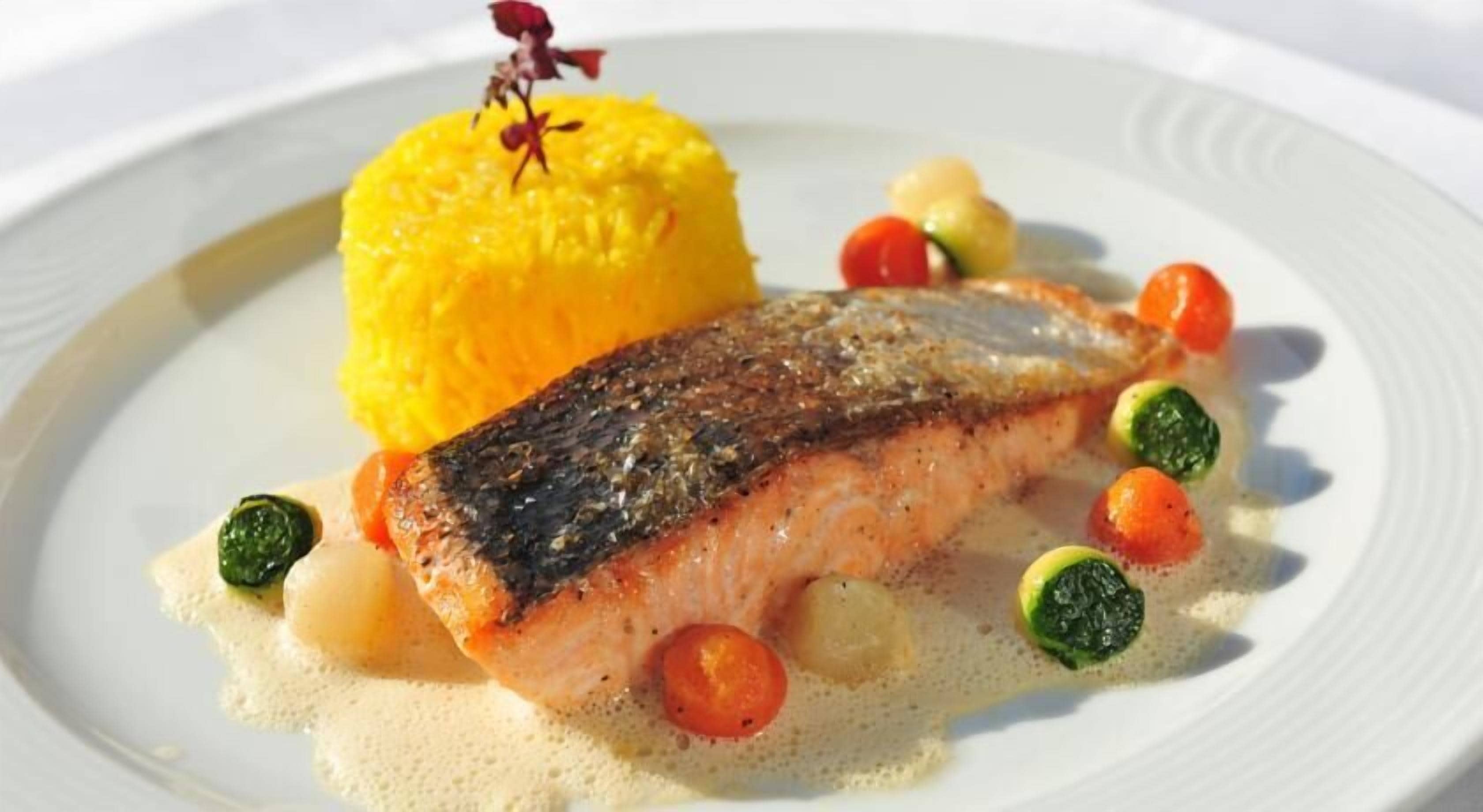 A plate with a piece of fish, yellow rice, and small vegetables.