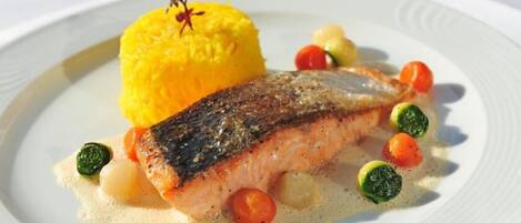 A plate with a piece of fish, yellow rice, and small vegetables.