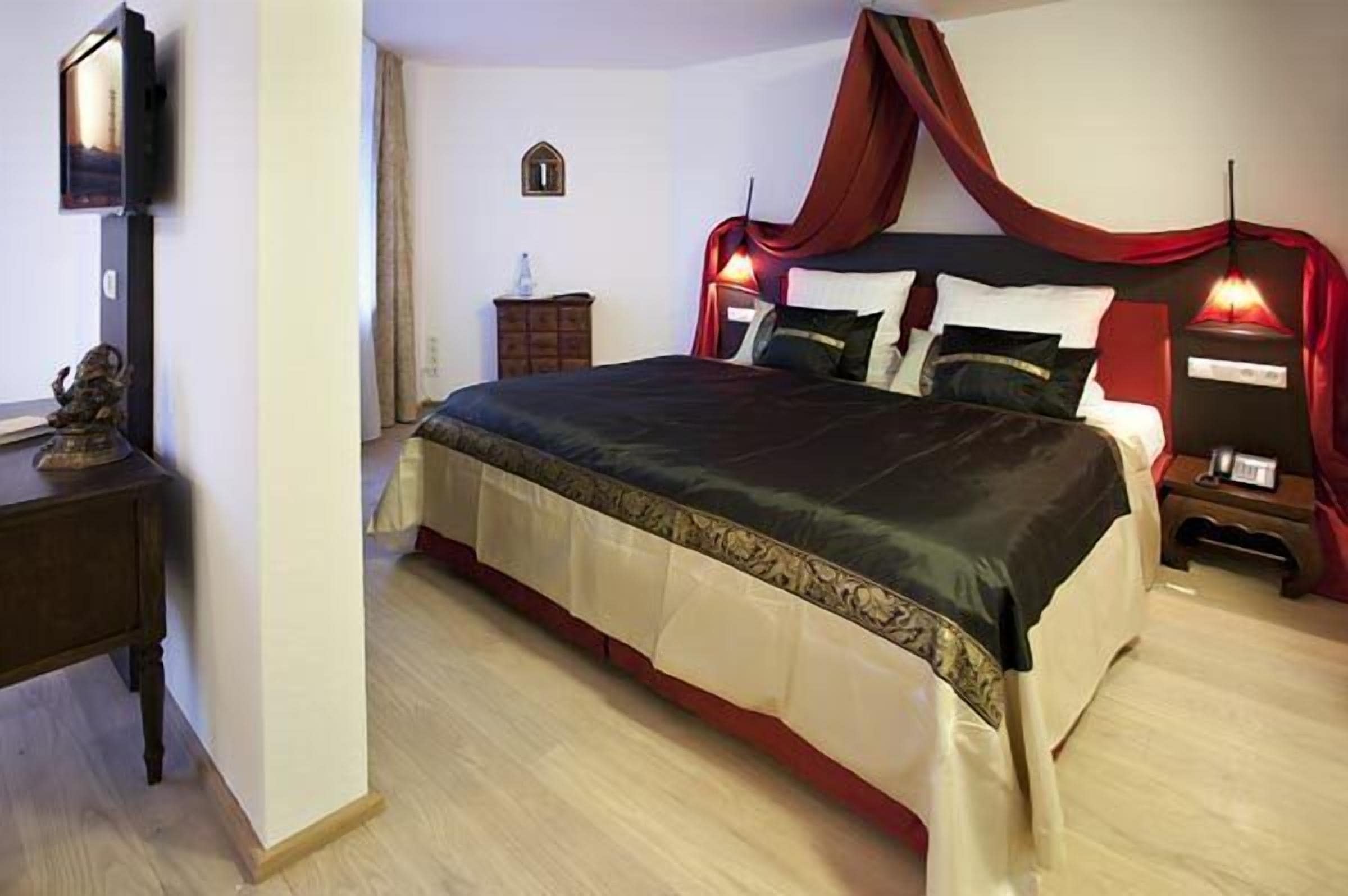 Un dormitorio con una cama grande, un televisor en la pared, una mesita de noche y un armario pequeño.