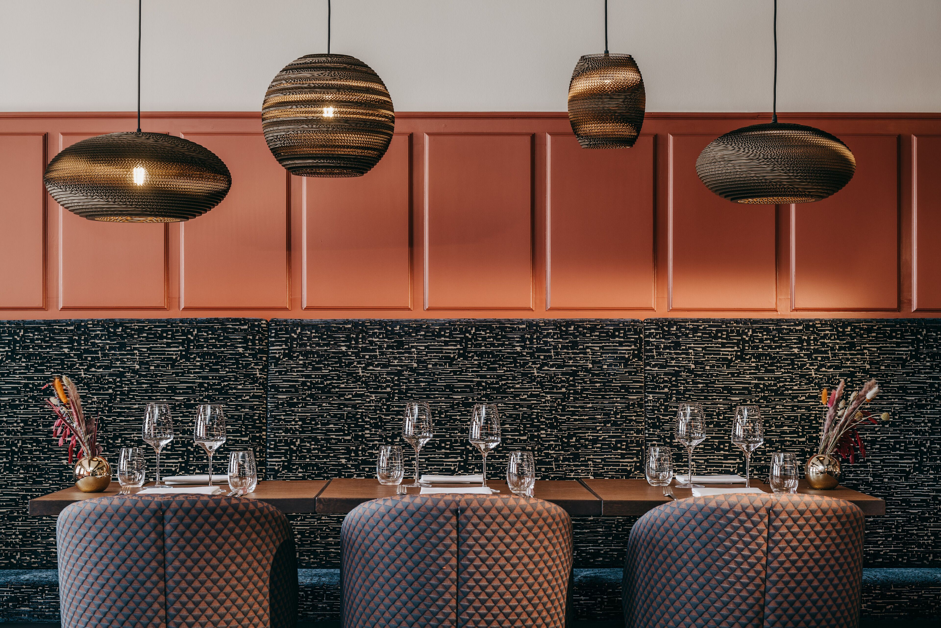 A dining area with a black textured wall, a wooden table set with glasses and cutlery, and patterned upholstered chairs.