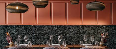 A dining area with a black textured wall, a wooden table set with glasses and cutlery, and patterned upholstered chairs.