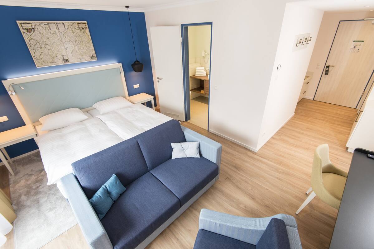 A modern hotel room with a large bed, a sofa, a desk, and a mirror.