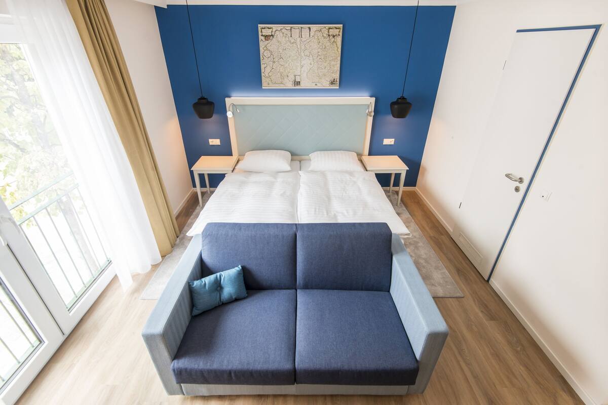 A modern bedroom with a large bed, a blue sofa, and a map artwork on the wall.
