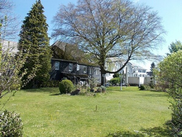 A residential property with a large lawn, a tall evergreen tree, and a two-story house with a dark exterior.