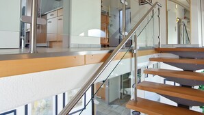 A modern interior with a staircase leading to a second floor, featuring glass railings and wooden steps. - Hotel Boeving (Breckerfeld)