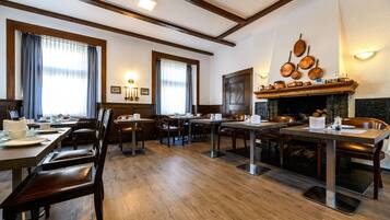 A dining area with wooden tables and chairs, a fireplace, and a wall-mounted pot rack.
