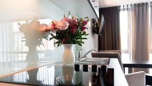 A modern kitchen with a glass countertop, a white vase with pink and white flowers, and a stainless steel sink. - Boardinghouse Bielefeld (Bielefeld)