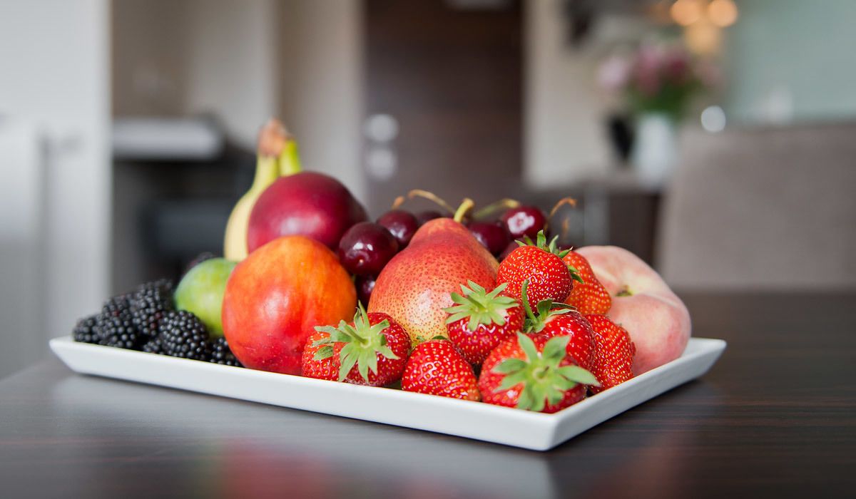 A white plate with a variety of fruits including strawberries, peaches, cherries, and blackberries.