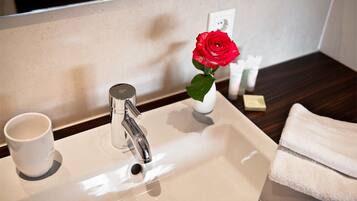 Un lavamanos de baño con un grifo moderno, una taza blanca y un florero con una rosa roja.