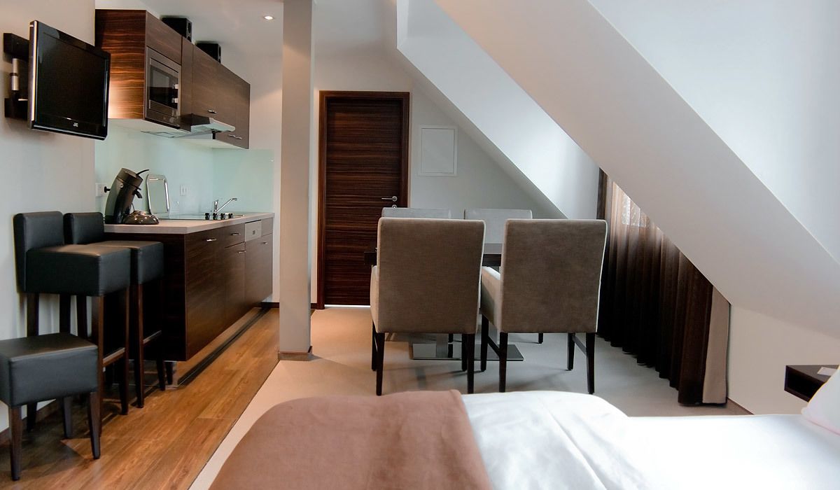 A modern hotel room with a kitchenette, a dining area with two chairs, a bed, and a staircase leading to an upper level.