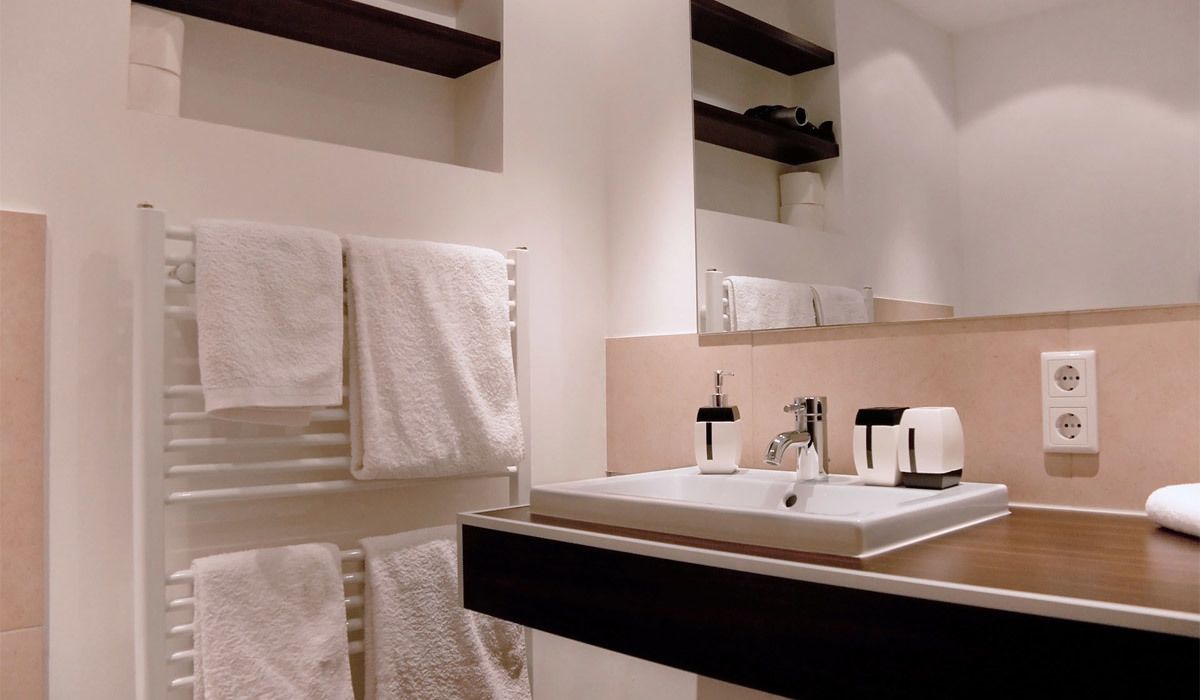 A modern bathroom with a white sink, black countertop, and a towel rack with multiple white towels.