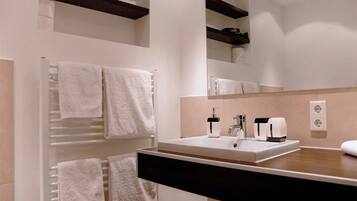 Ein modernes Badezimmer mit einem weißen Waschbecken, einer schwarzen Ablagefläche und einem Handtuchhalter mit mehreren weißen Handtüchern.