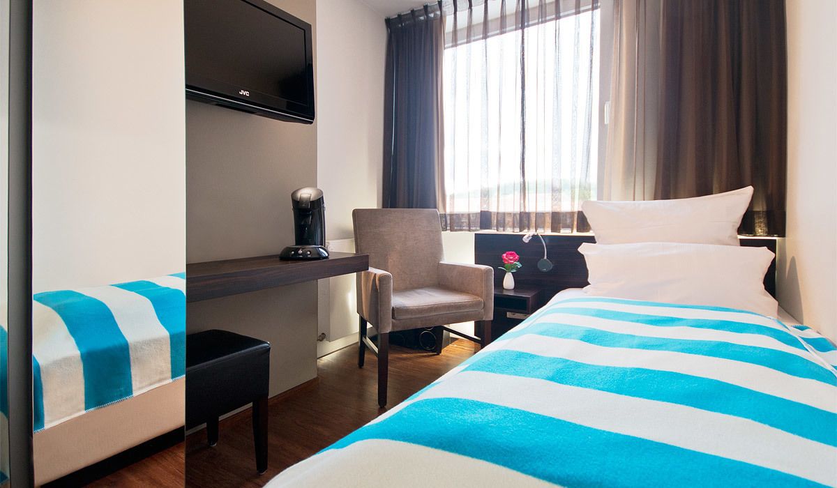 A hotel room with a bed, a desk, a chair, a TV, and a window with curtains.