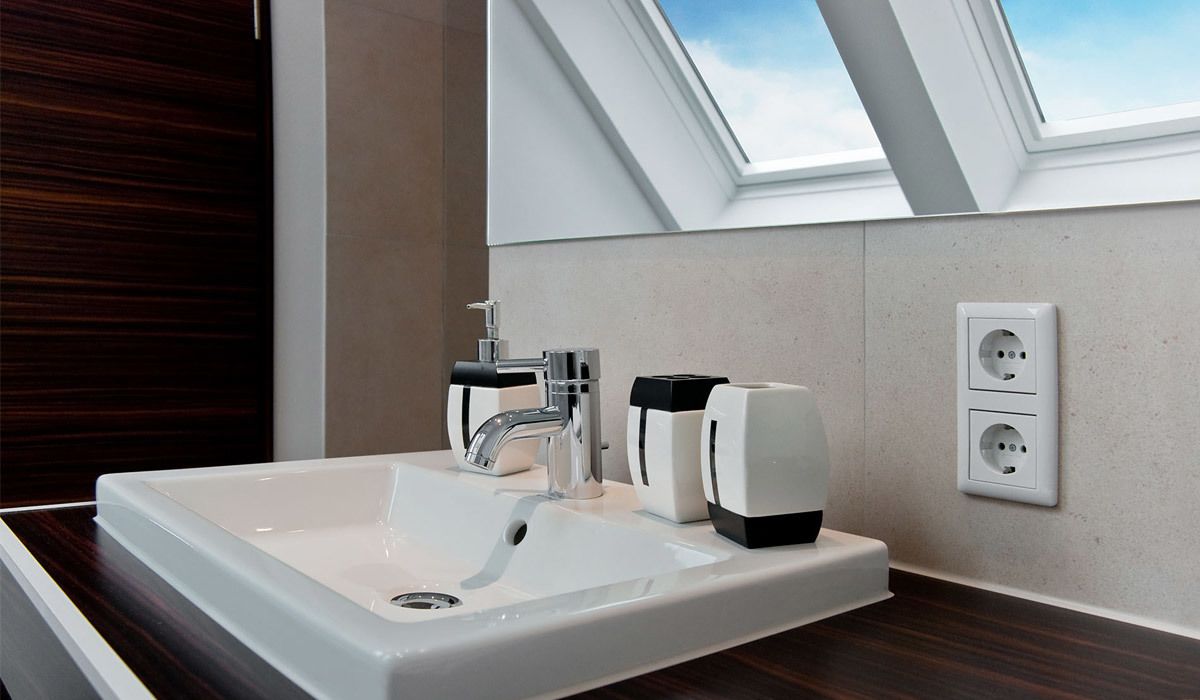 Un baño moderno con un lavamanos blanco grande, un grifo elegante y un dispensador de jabón integrado. Se observa un tragaluz sobre el lavamanos, y una toma de corriente en la pared.