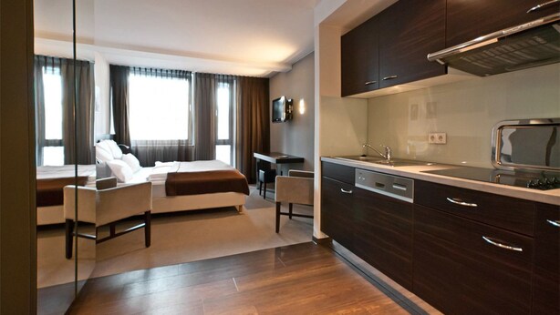 A modern hotel room with a bed, seating area, kitchenette, and a large window with curtains. - Boardinghouse Bielefeld (Bielefeld)