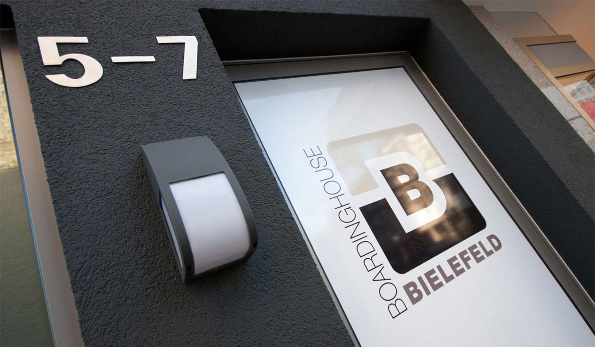 A hotel entrance with a sign indicating room number 5-7 and the name 'BOARDINGHOUSE BIELEFELD'.