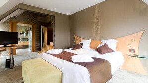 Habitación de hotel moderna con una cama grande, televisor y baño visible a través de una puerta abierta.