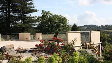A rooftop terrace with a view of the countryside, a pergola, and a variety of plants.
