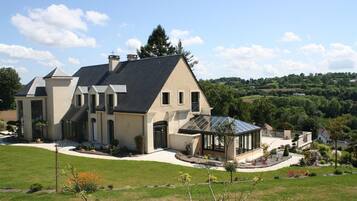A large, modern house with a spacious front yard, a covered patio, and a view of the surrounding countryside.