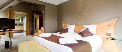 Ein modernes Hotelzimmer mit einem großen Bett, einem Fernseher und einem durch eine geöffnete Tür einsehbaren Badezimmer.