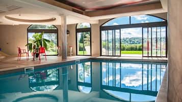 A swimming pool with a view of the outdoors, a seating area with chairs, and a large window.