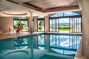Piscina con vistas al exterior, zona de estar con sillas y un amplio ventanal.