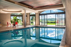 Piscina com vista para o exterior, área de estar com cadeiras e uma janela grande.