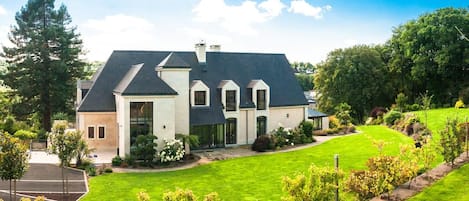 Une grande maison avec une pelouse bien entretenue, une allée et une variété d’arbres et d’arbustes.