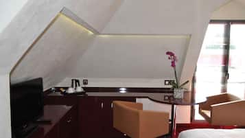 A hotel room with a television, a desk with a coffee maker, a chair, a bed, and a window with a view.