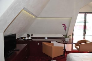 Habitación de hotel con televisión, escritorio con cafetera, una silla, cama y ventana con vistas.