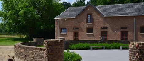 A brick building with a pitched roof, a paved courtyard, and a stone wall with circular cutouts.