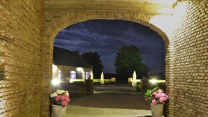 Uma entrada de tijolos em arco para um edifício à noite, com duas plantas em vasos e iluminação externa.