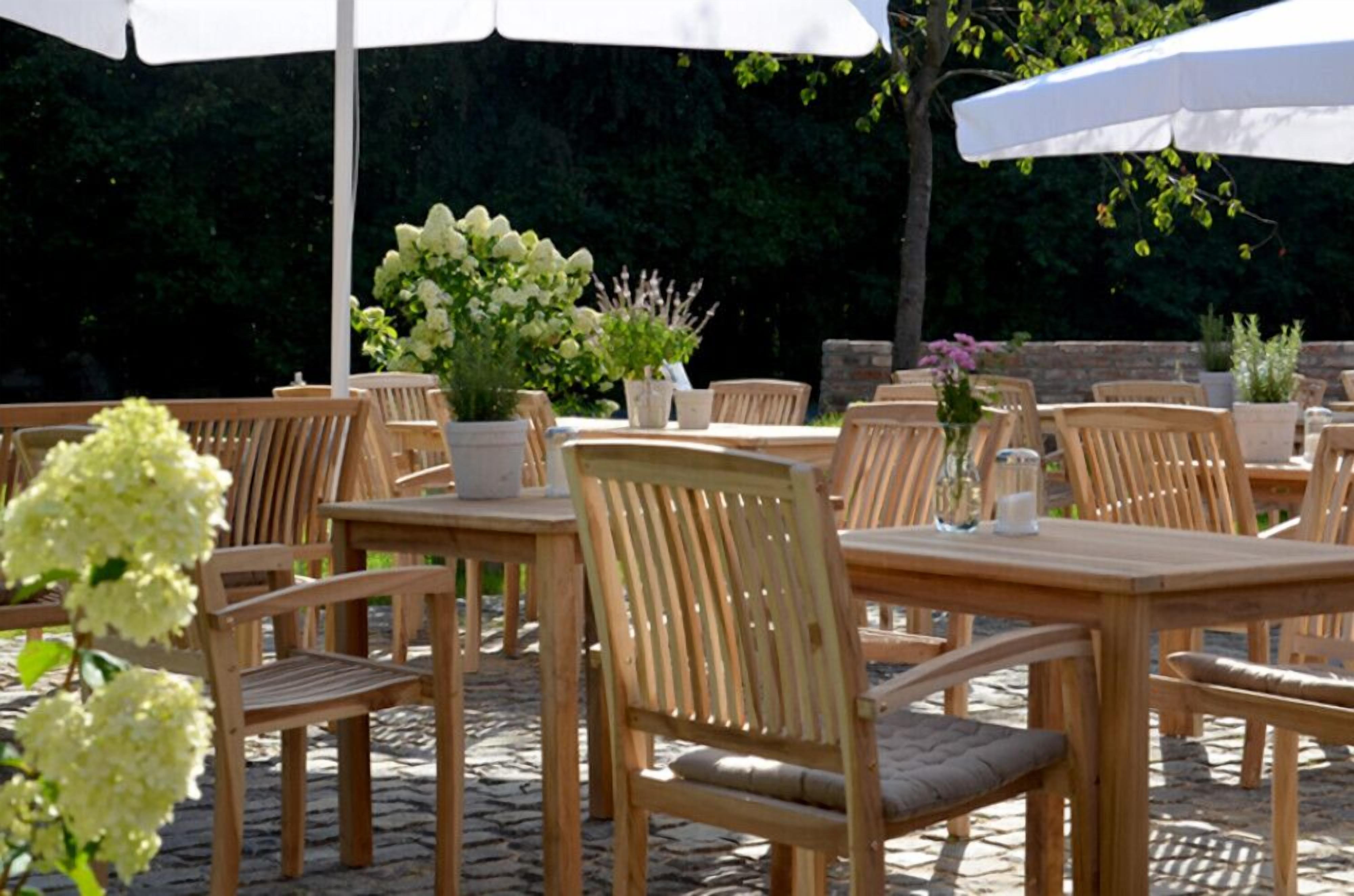 An outdoor patio with wooden tables and chairs, white umbrellas, and potted plants.