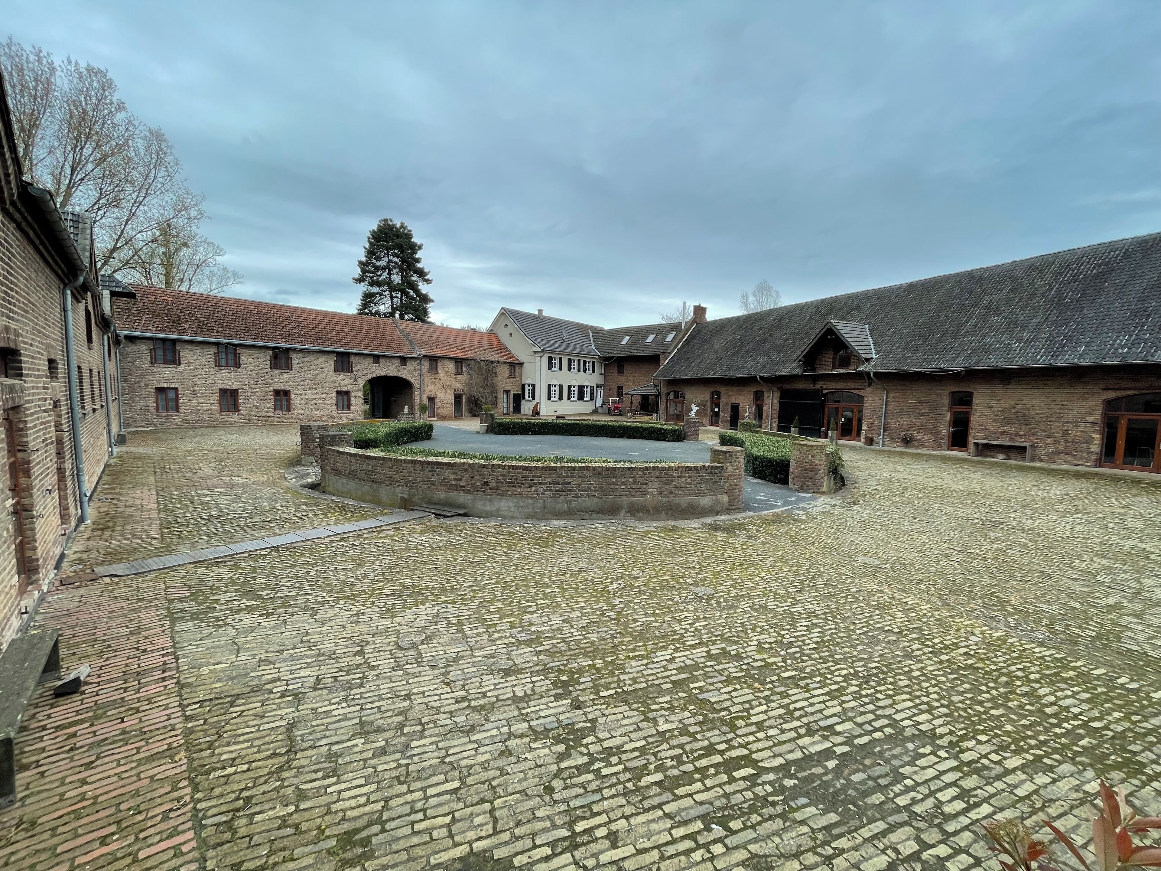 A courtyard with cobblestone flooring, surrounded by traditional brick buildings with dormer windows and a central water feature.