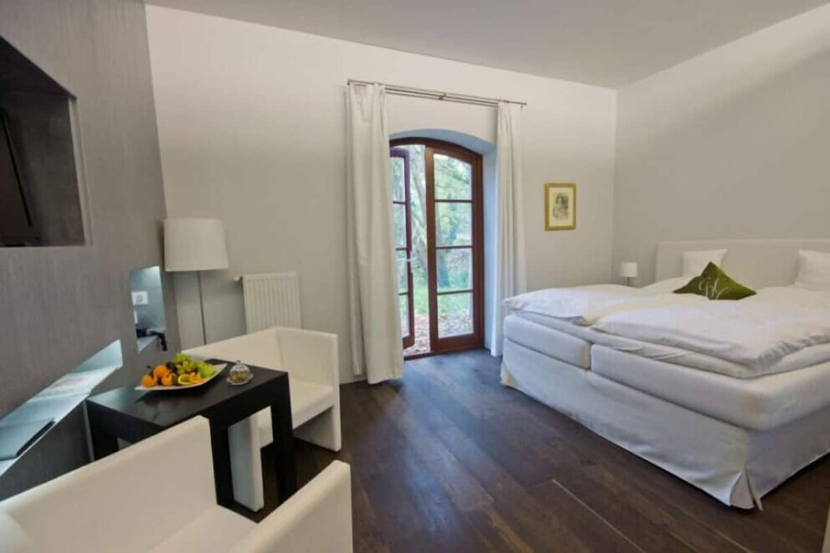 A hotel room with a bed, a desk with a lamp, a chair, and a view of the outdoors through a window.
