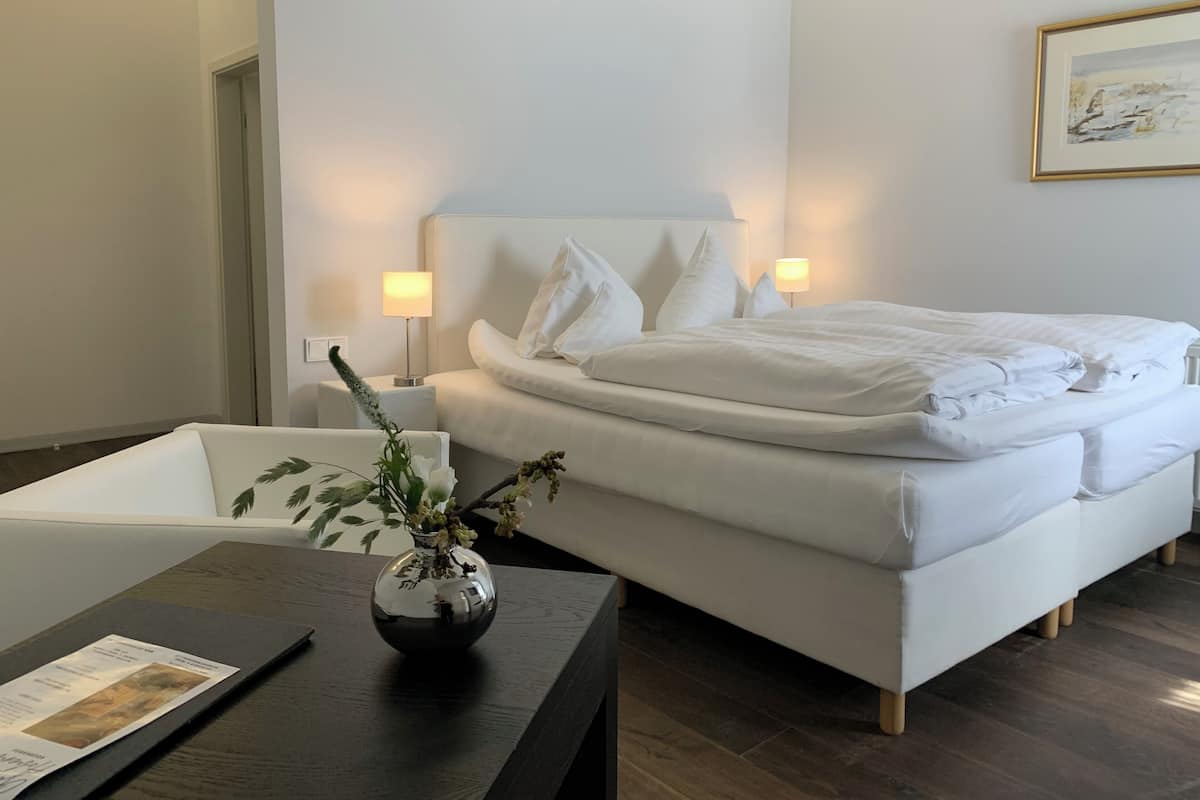 A modern hotel room with a neatly made bed, a bedside table with a vase of flowers, and a lamp.