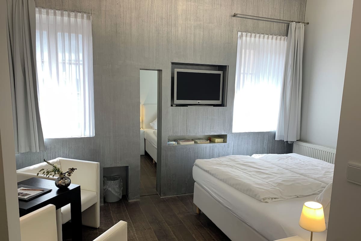 A modern hotel room with a bed, a desk, a chair, a TV, and a lamp.