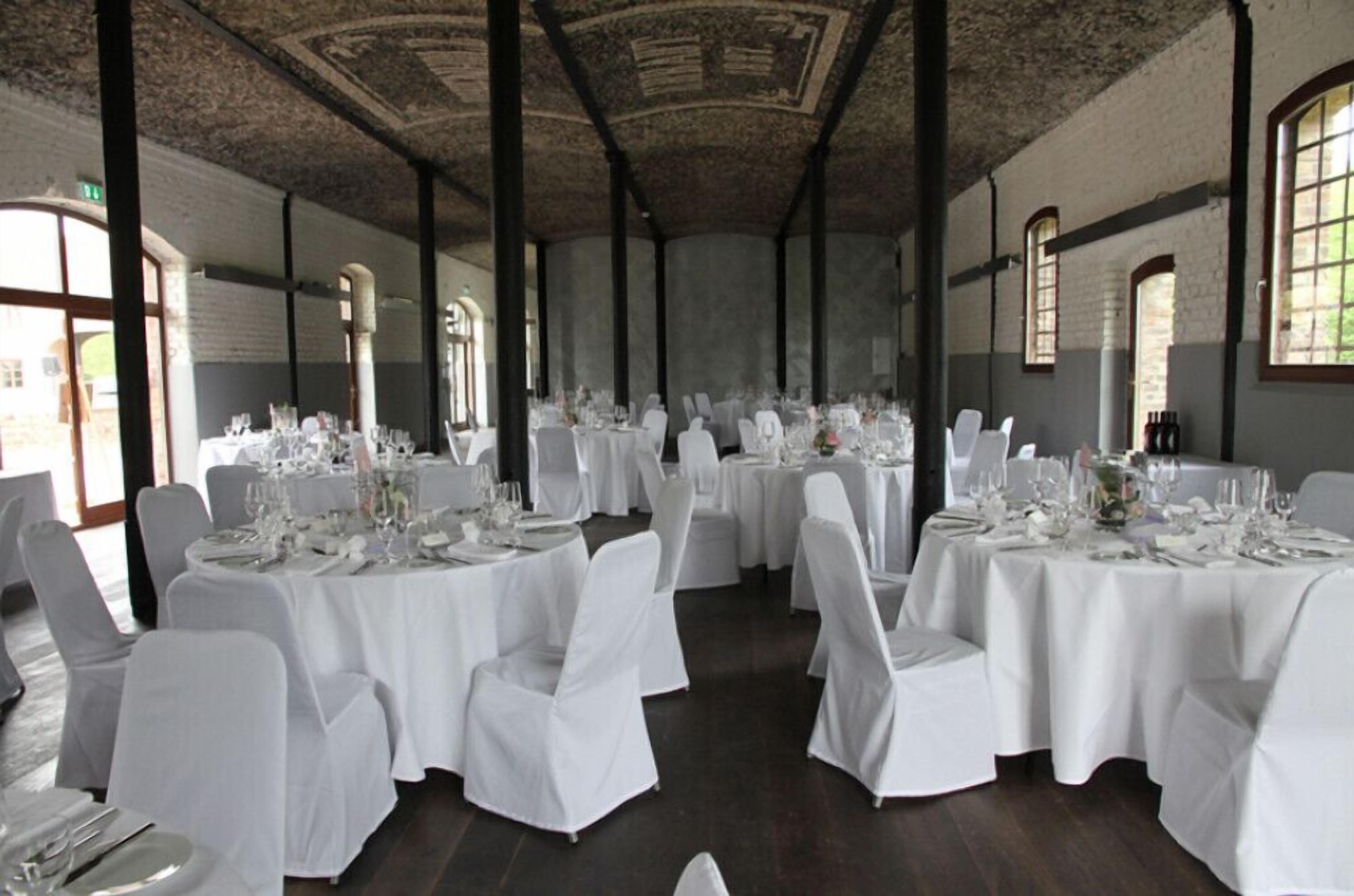 A banquet hall with round tables set for a formal event, featuring white tablecloths and chairs, and a high ceiling with decorative elements.