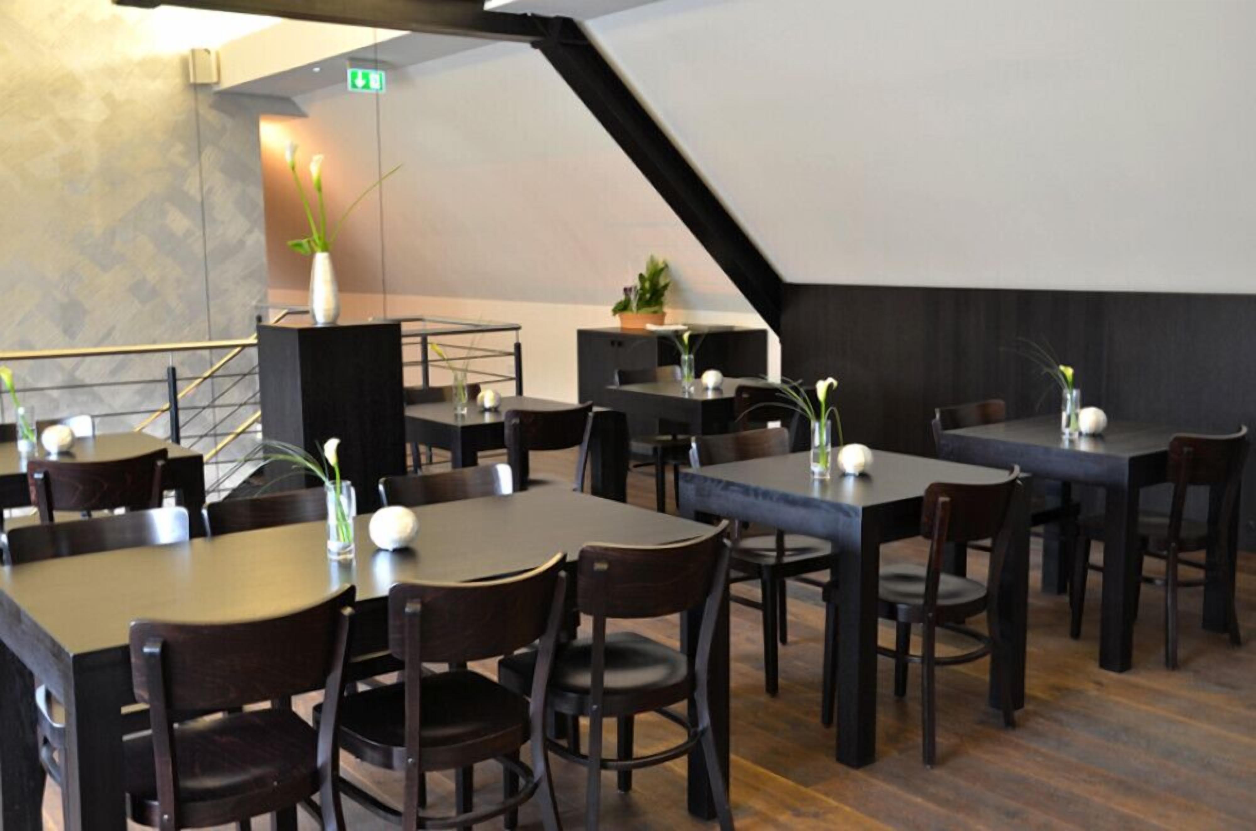 A restaurant with dark wooden tables and chairs, a staircase, and a modern interior design.