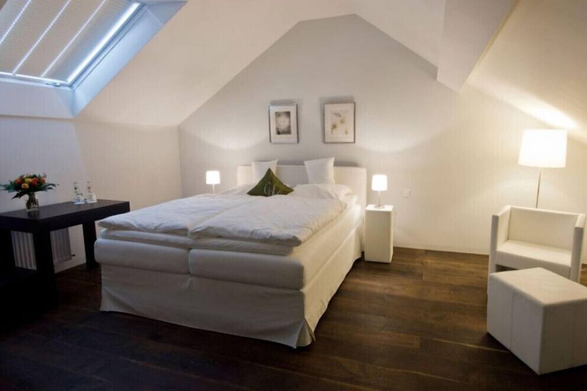 A bedroom with a skylight, a bed, bedside lamps, a small table with a vase, and a chair.