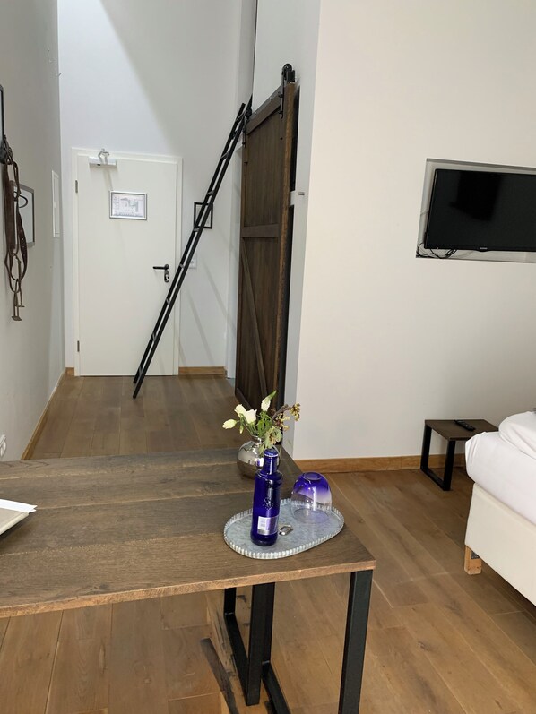 A wooden table with a vase of flowers, a TV mounted on the wall, and a staircase in the background. - Gut Hohenholz (Bedburg)