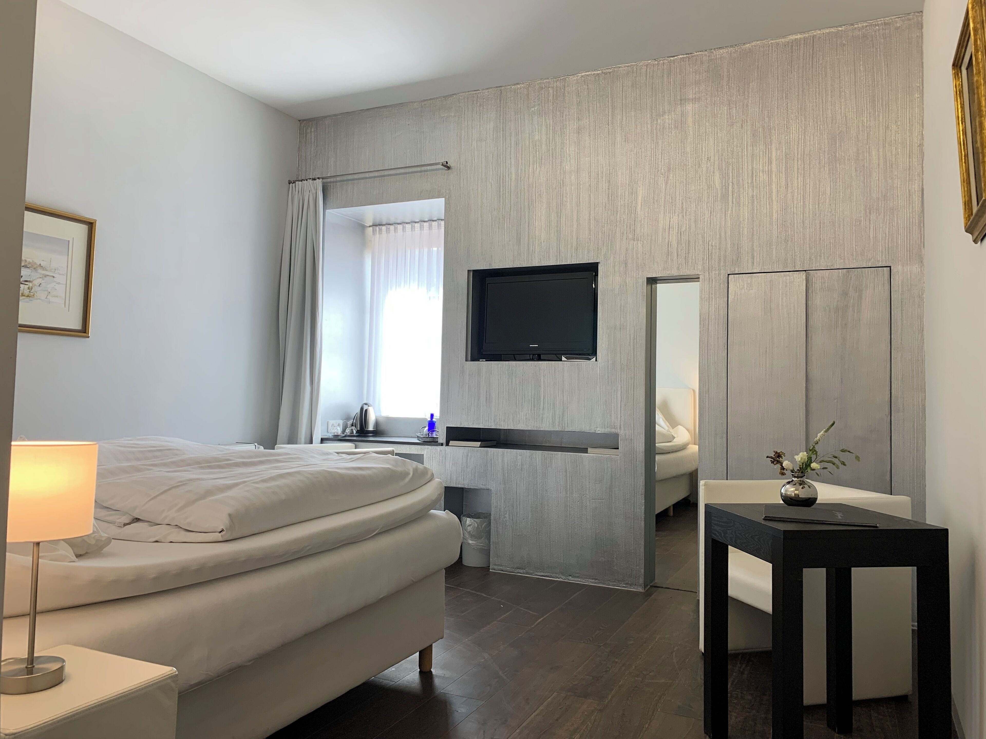 Una habitación de hotel moderna con cama, mesita de noche, lámpara, televisión y una pequeña mesa con un florero.
