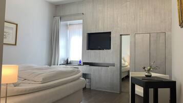 Una habitación de hotel moderna con cama, mesita de noche, lámpara, televisión y una pequeña mesa con un florero.
