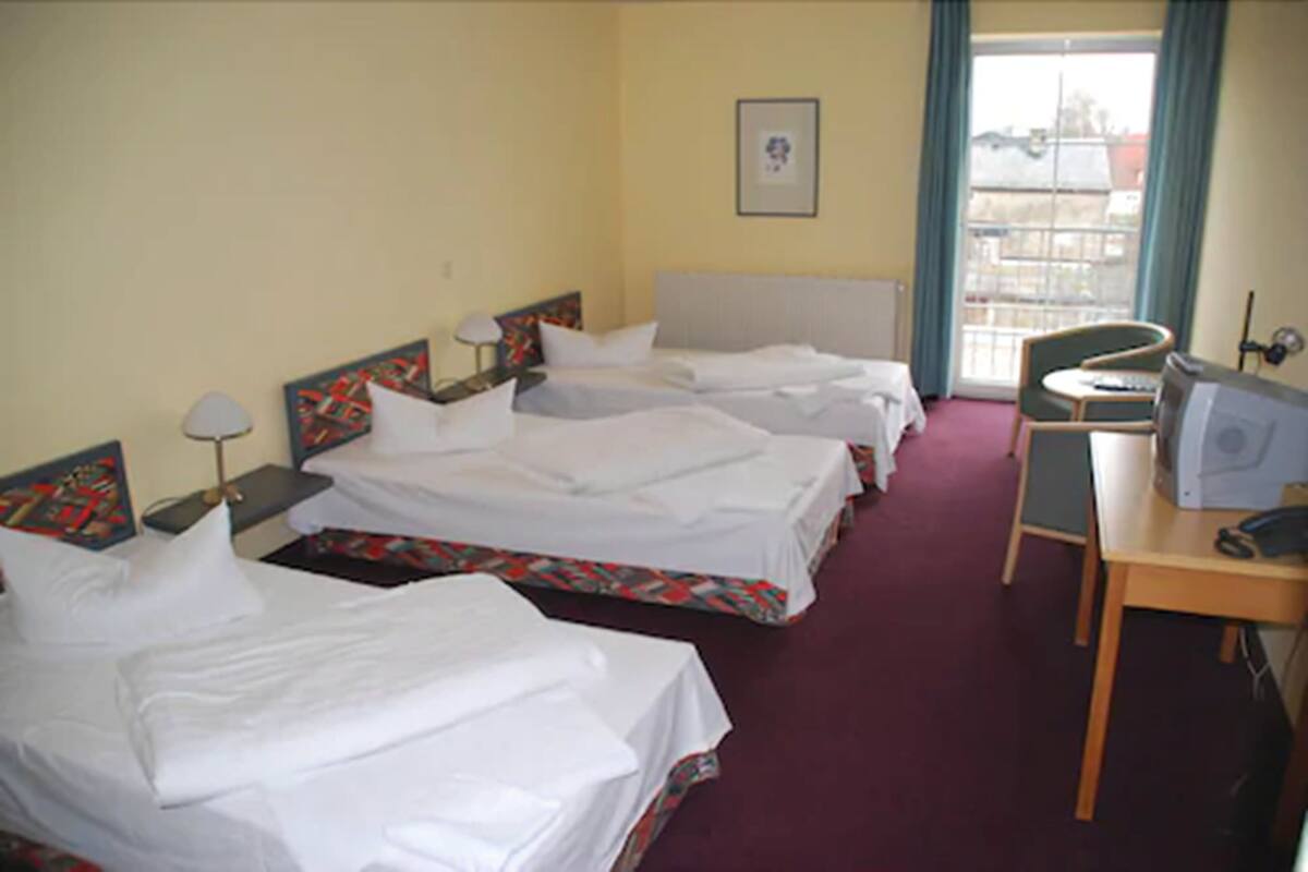 A hotel room with three beds, a desk with a computer, and a window with curtains.