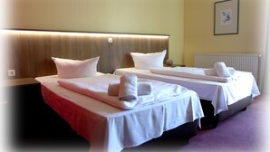 A hotel room with two single beds, each with a white bedspread and pillows, and a headboard with built-in lighting. - Hotel Lindenberger Hof (Ahrensfelde)