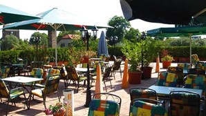 An outdoor patio with tables and chairs, umbrellas, and potted plants. - Hotel Lindenberger Hof (Ahrensfelde)