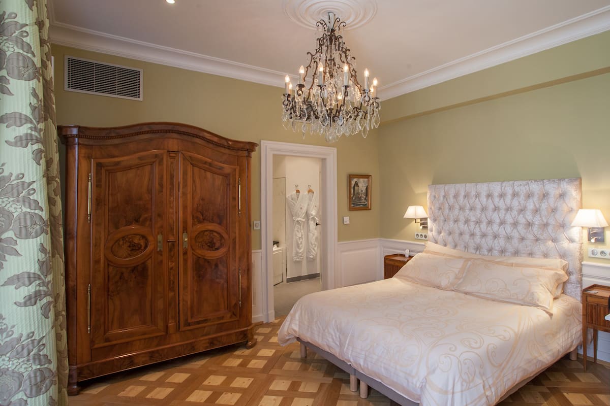 Quarto com um armário de madeira grande, cabeceira estofada e um candelabro.
