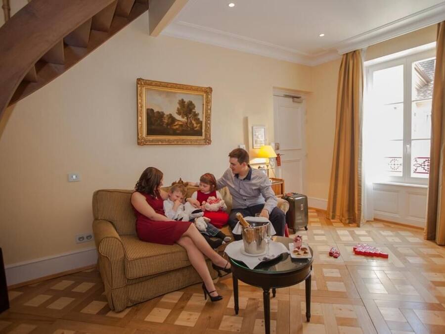 Una sala de estar con una escalera de madera, un sofá, una mesa de comedor con una botella de champán y un cuadro en la pared.