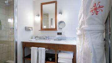 A bathroom with a glass shower enclosure, a wooden vanity with a marble countertop, a large mirror, and a robe with a red design.