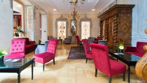 A spacious living room with red upholstered chairs, a large wooden cabinet, and a chandelier. - Hotel & Spa Le Bouclier D'Or (Strasbourg)
